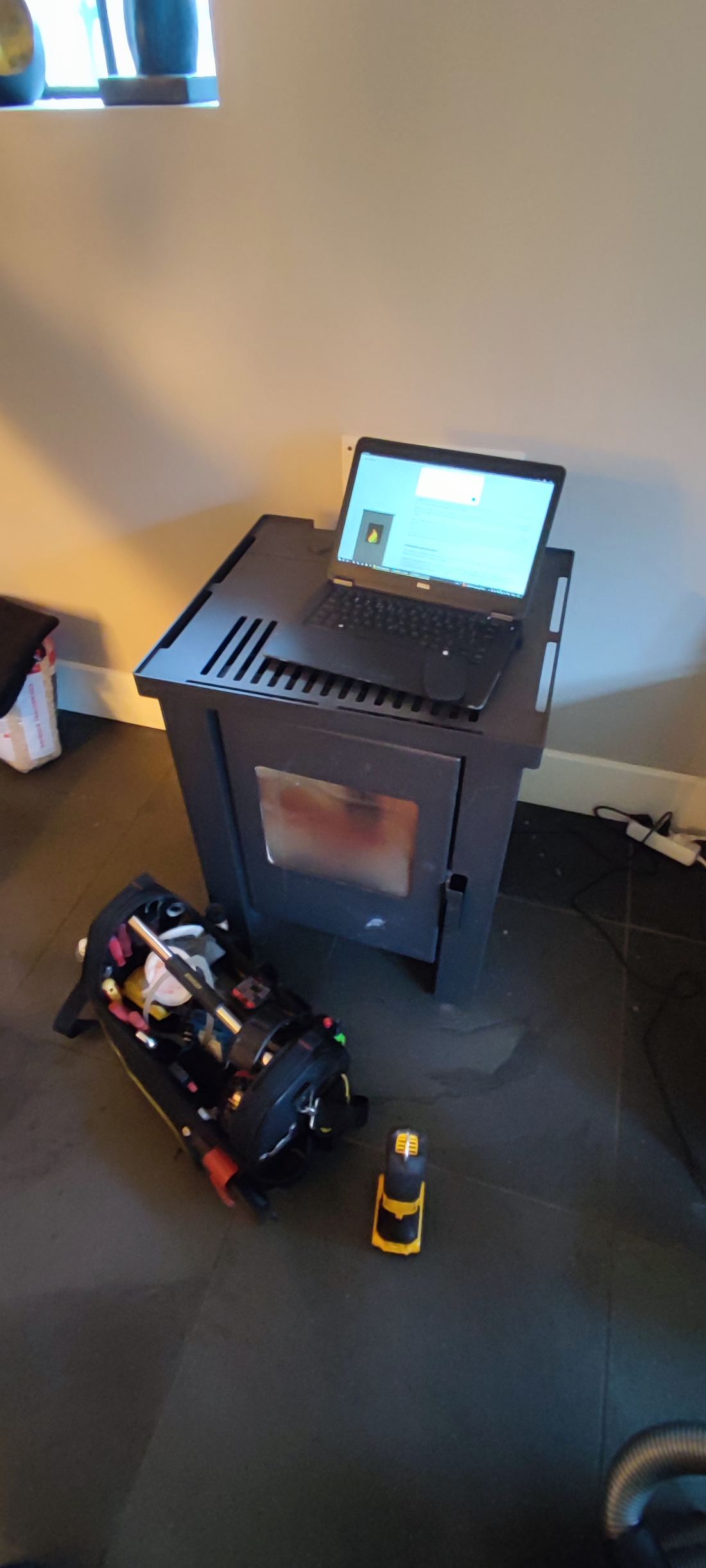 Laptop met uitleessoftware op een pelletkachel, gereedschapstas ervoor